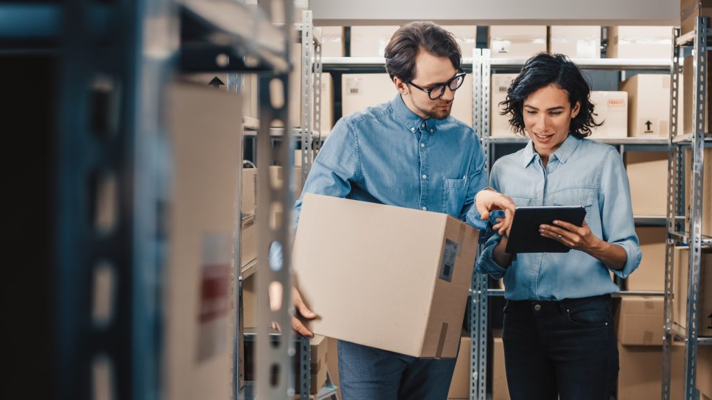 Workers in a packaging warehouse reviewing order details on a tablet